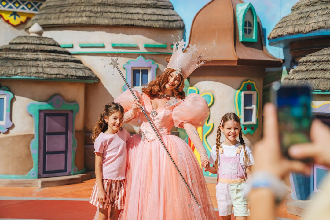 A woman in a pink fairy costume holding a wand with two children