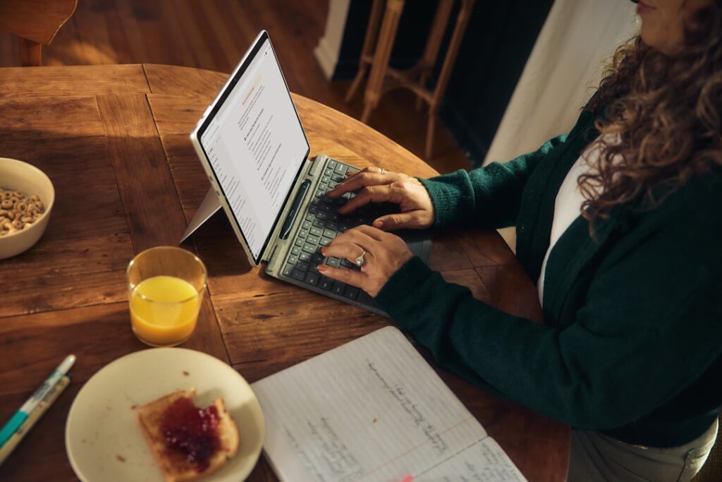 Woman typing on laptop at wooden table with breakfast