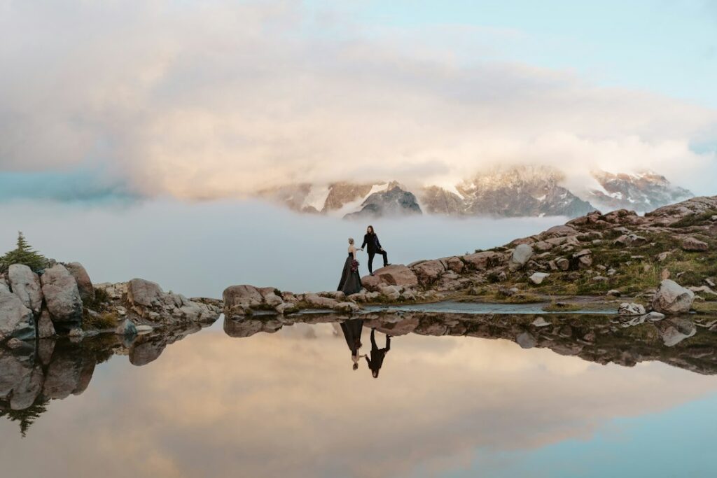 Couple standing on rocks by calm mountain lake reflection